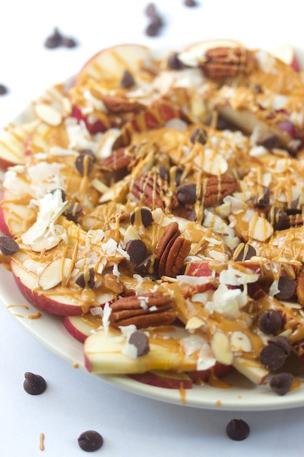 crisp apple slices drizzled with peanut butter and topped with pecans, coconut flakes and chocolate chips