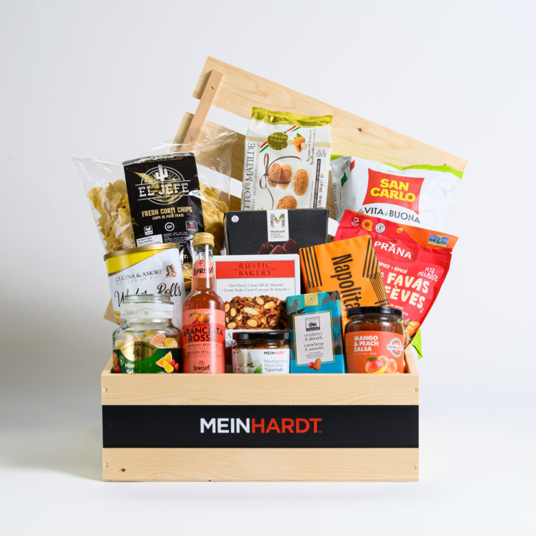 Wooden crate gift basket with "Meinhardt" written on the front. With packaged sweet treats, snacks and drinks inside backed by another wooden crated board.