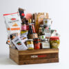wooden crate with dark stain with Meinhardt written on it, containing about 27 food snacks, treats and 2 drinks.