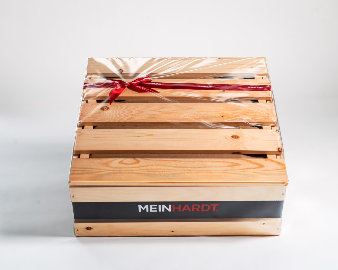 Cellophane wrapped Wooden Gift basket with a red ribbon going around it. Front facing is Black stripped painted line with Meinhardt written on it.