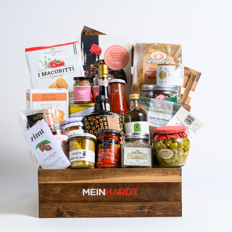 wooden crate with dark stain with Meinhardt written on it, containing about 27 food snacks, treats and 2 drinks.