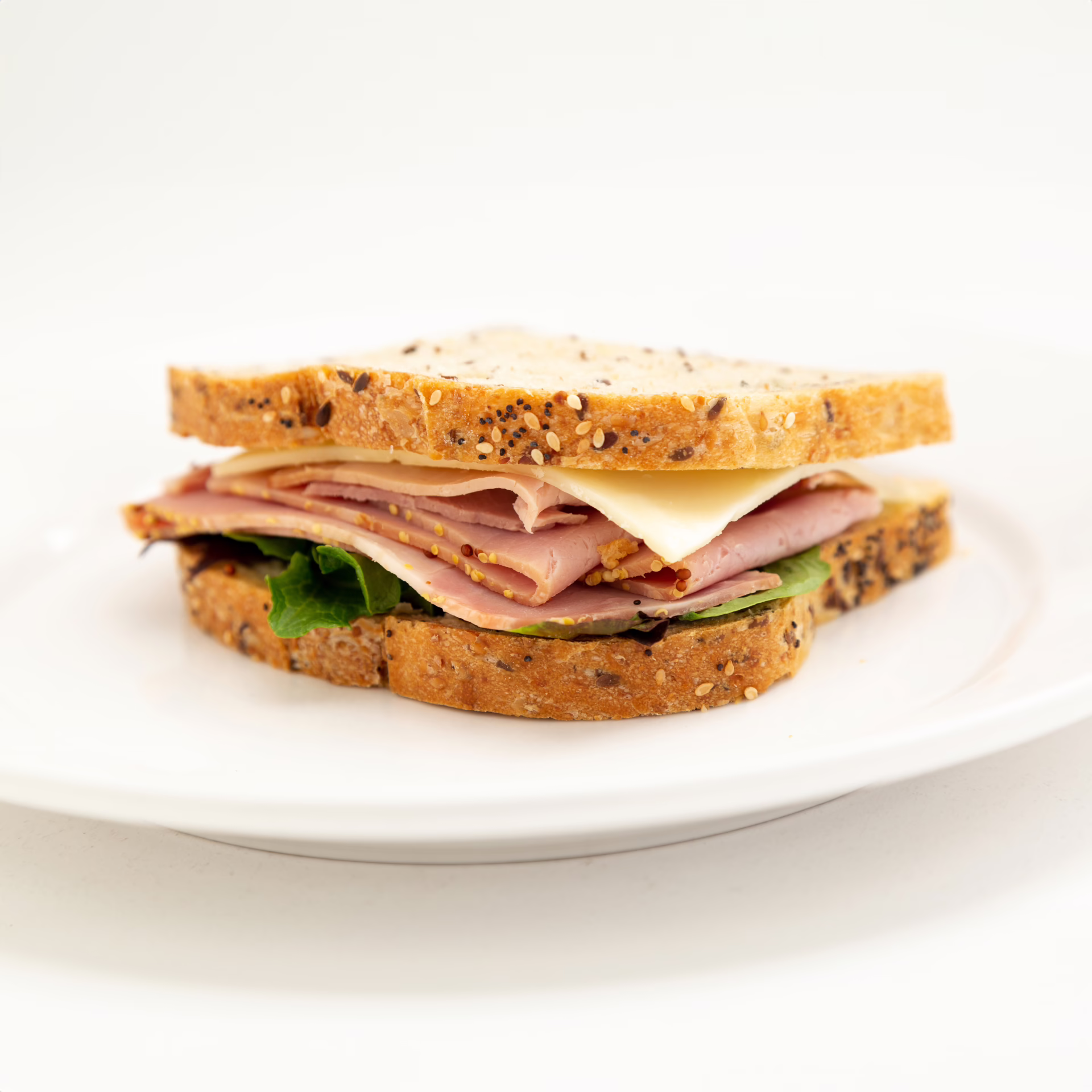 Whole Wheat nuts Bread with Honey Ham, Cheese, Spinach, Dijon Mayo presented on a white plate