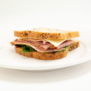 Whole Wheat nuts Bread with Honey Ham, Cheese, Spinach, Dijon Mayo presented on a white plate